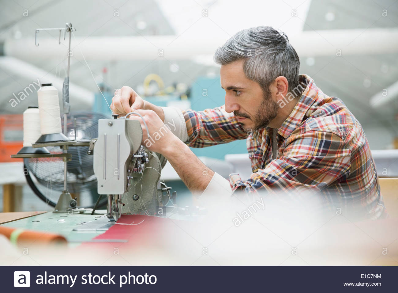 Worker using sewing machine in textile manufacturing plant Stock Photo