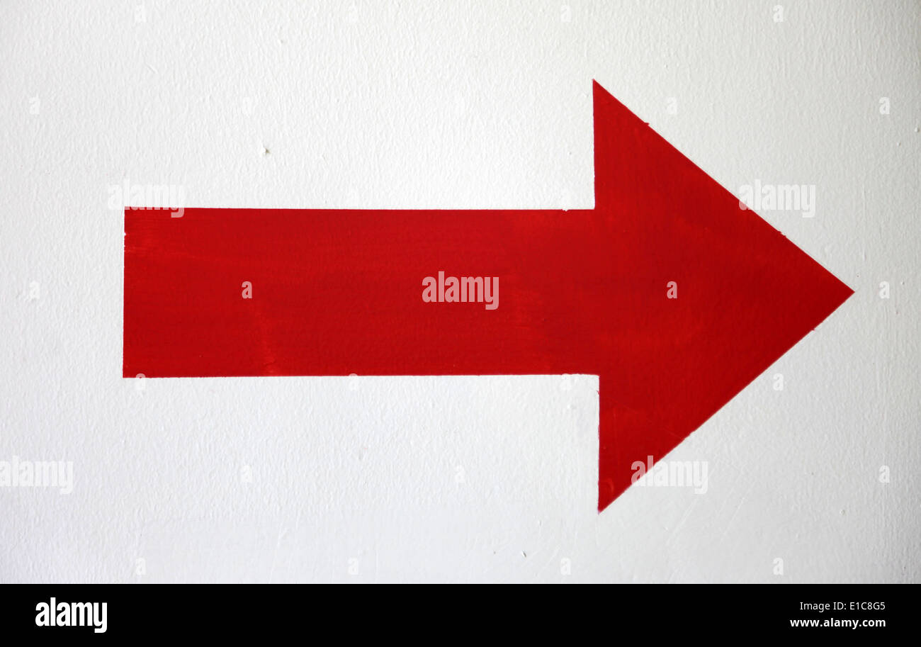 It's a photo of a red arrow that show the right direction. It's a large arrow painted against the white wall indoor or inside Stock Photo