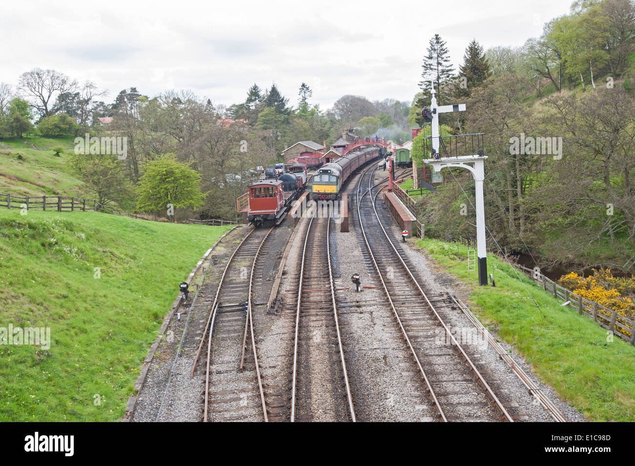 Old english traditional railway station with train on tracks through rural countryside scenery Stock Photo