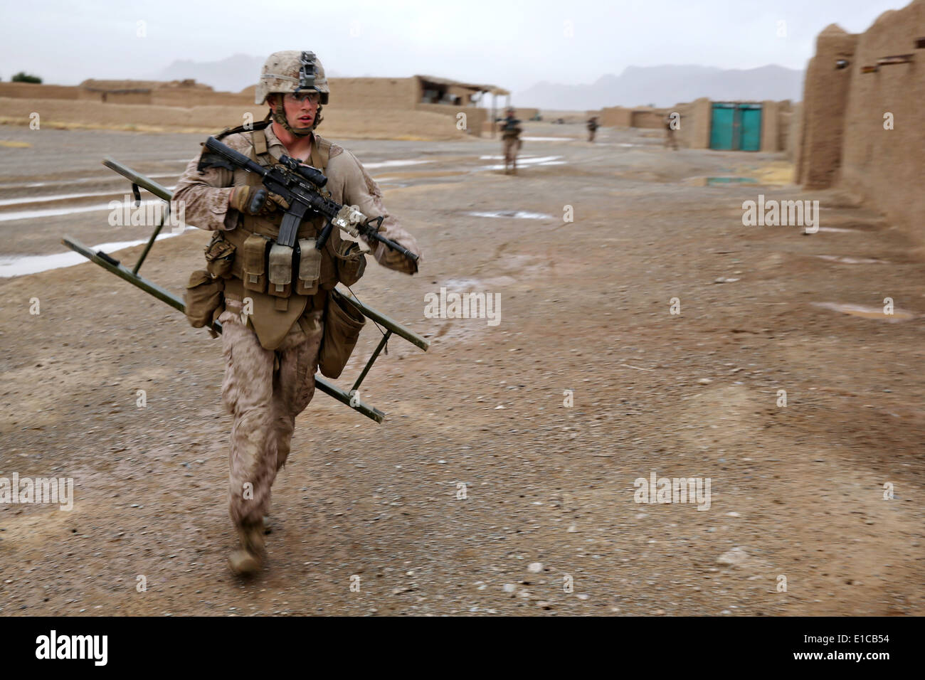 A US Marine with the 1st Battalion, 7th Marine Regiment, runs to provide a combat ladder to a fellow Marine searching a compound May 16, 2014 in Larr Village, Helmand province, Afghanistan. Stock Photo