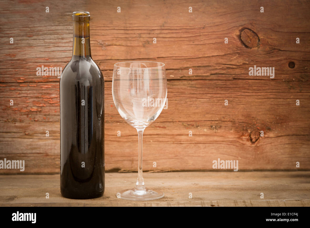 Wine bottle with the label removed standing alongside an elegant wineglass against rustic wooden boards with copy space Stock Photo
