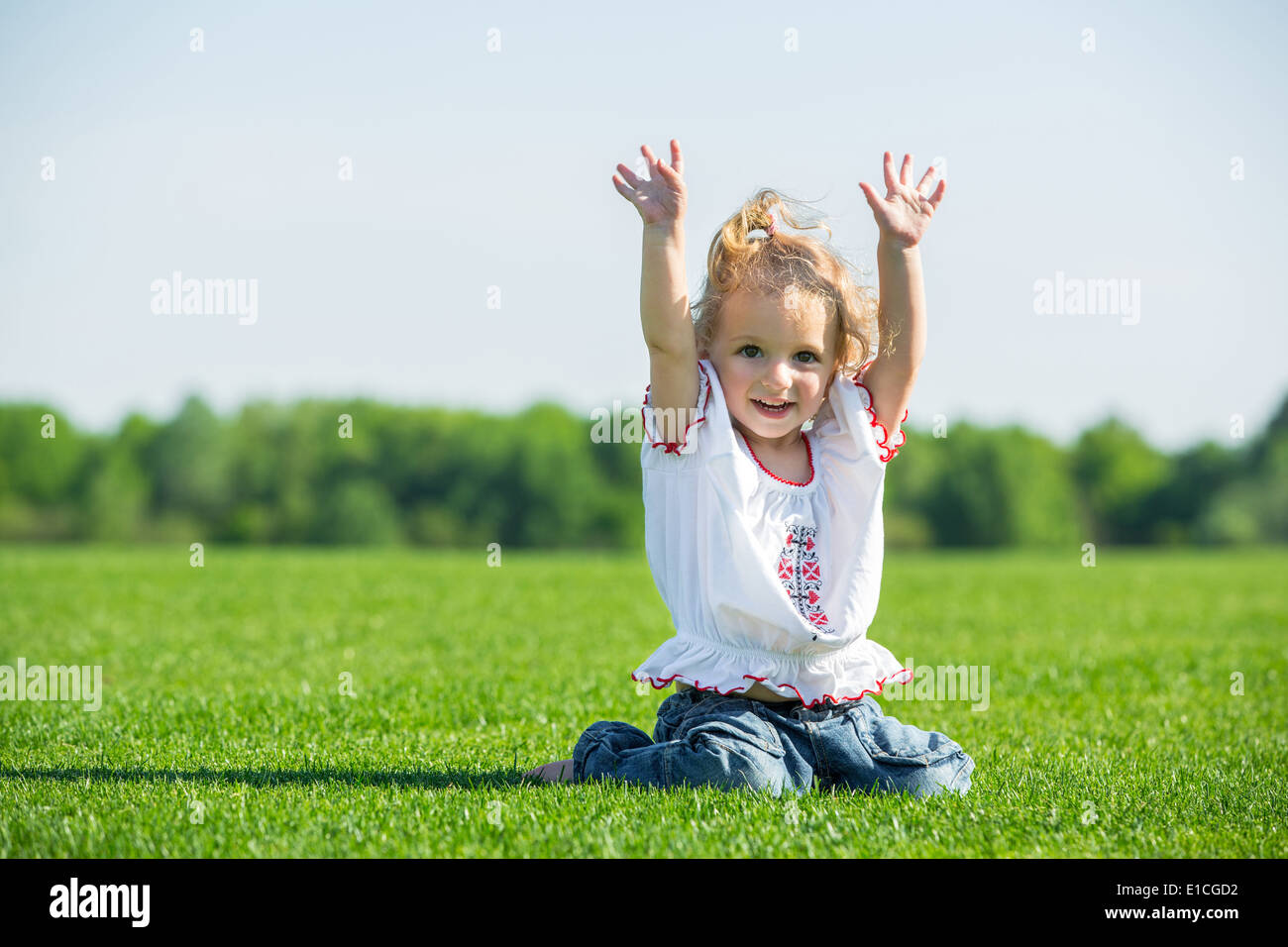 Cute smiling little girl sitting on a fresh green grass in a field ...