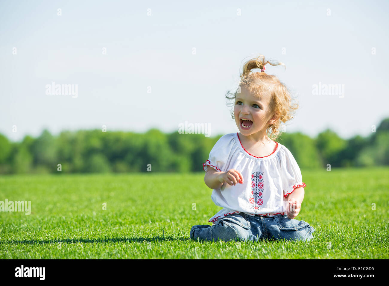 Cute smiling little girl sitting on a fresh green grass in a field ...