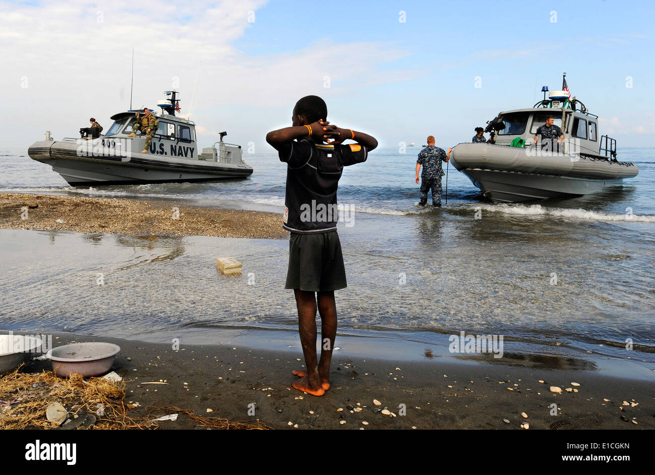 A Haitian boy watches as U.S. Sailors in rigid-hull inflatable boats from the amphibious dock landing ships USS Fort McHenry (L Stock Photo