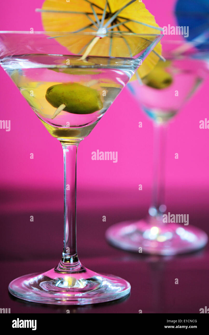 Two martinis with olives and colorful umbrellas against a pink backdrop Stock Photo