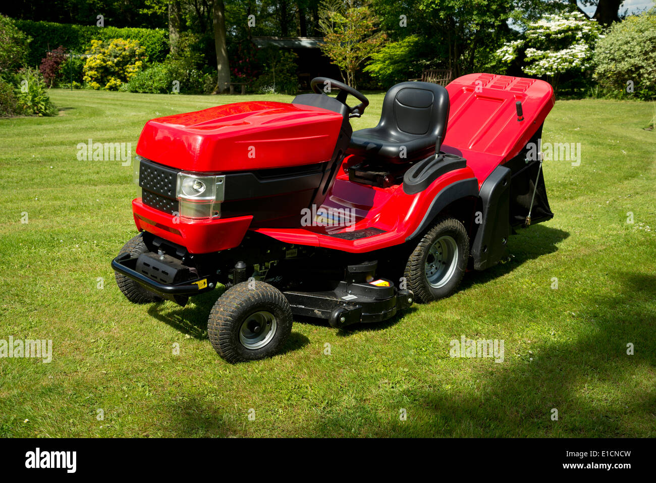 Red garden tractor, or ride on mower, in an verdant garden. Stock Photo