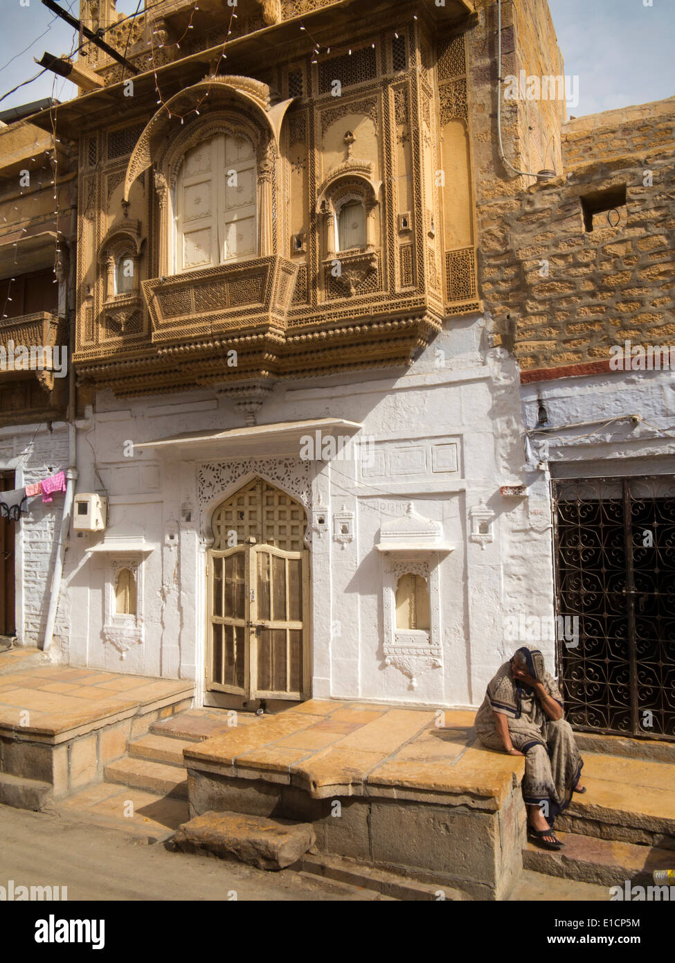 India, Rajasthan, Jaisalmer, woman sat outside decoratively carved sandstone façade house Stock Photo