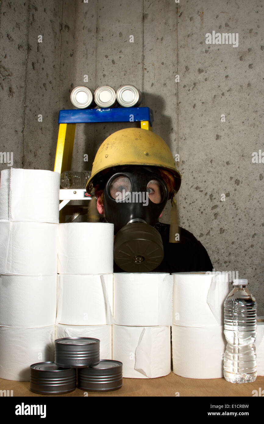 Woman dressed in gas mask and hard hat hiding in the basement with stockpiled goods Stock Photo