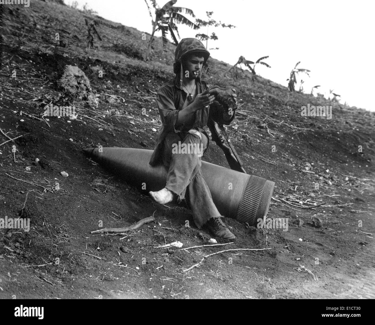 A Marine sits on an 16-inch naval shell to shake a three-days of sand from his boots. Battle of Saipan battle against the Stock Photo