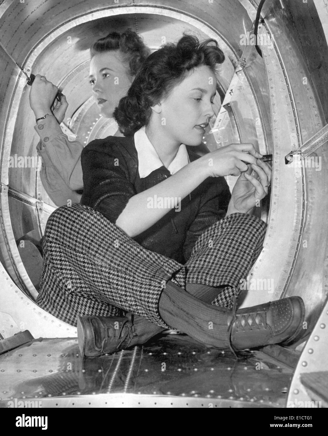 Two women workers in a cramped aircraft space at Grumman Aircraft Engineering Corp. During World War 2, ca. 1942-45. Stock Photo