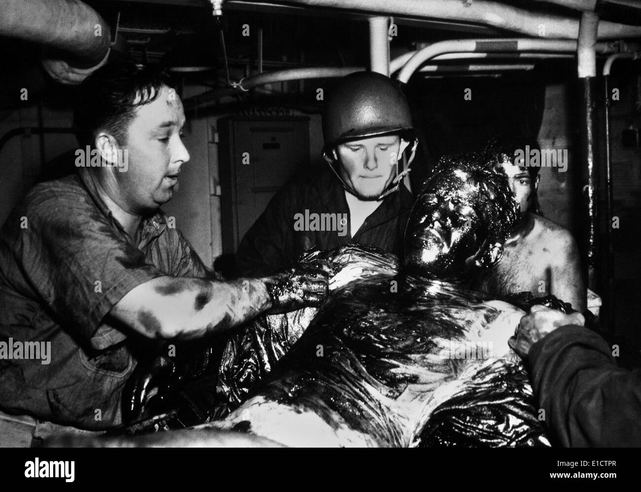 Coast Guardsmen scrape a thick coating of oil from the body of U.S. Navy seaman. His ship USS LANSDALE, was sunk by Nazi planes Stock Photo