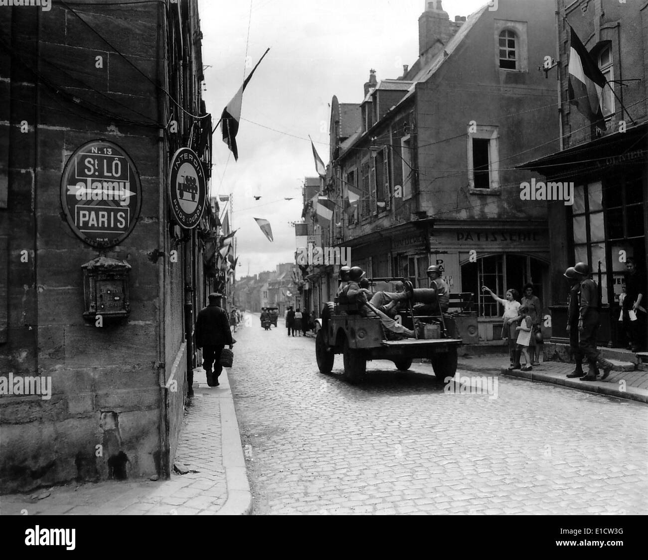 Five U.S. soldier ride through Carentan, France, on the road to Saint-Lo, June 12, 1944. French flags decorate the street of Stock Photo