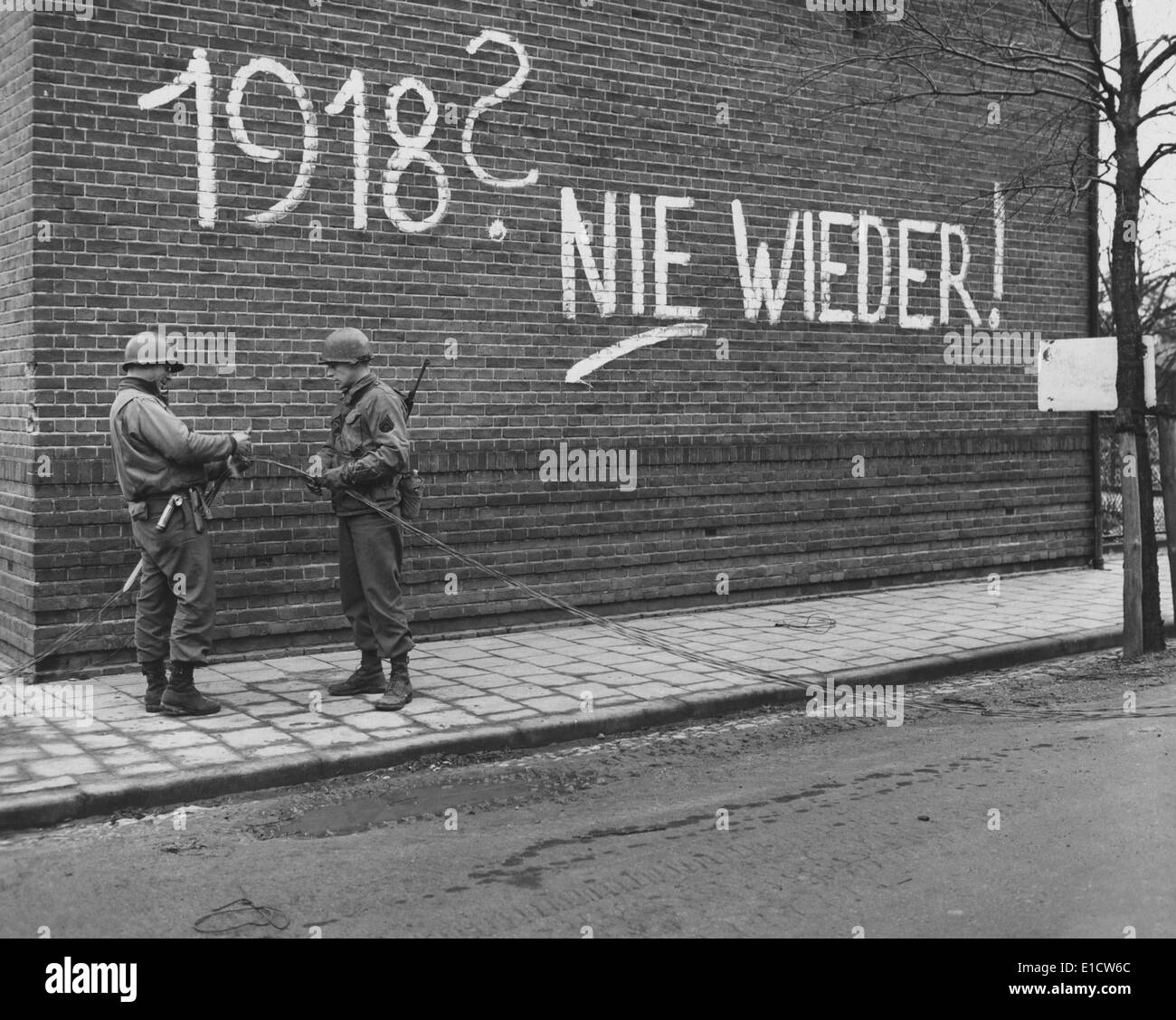 U.S. Ninth Army signalmen repair wires near German graffiti in the Netherlands. It reads, '1918, Never More', referring to the Stock Photo