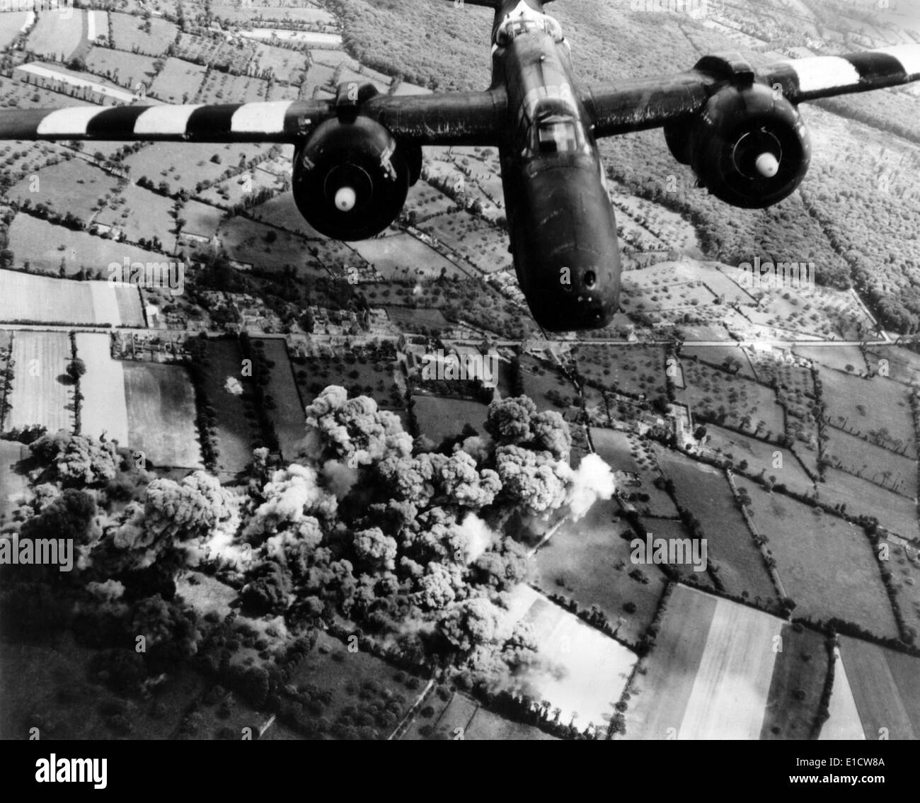 Aerial view of a A-20 G Havoc light bomber with D-Day 'invasion stripes' painted on its wings. Plumes of smoke rise from the Stock Photo