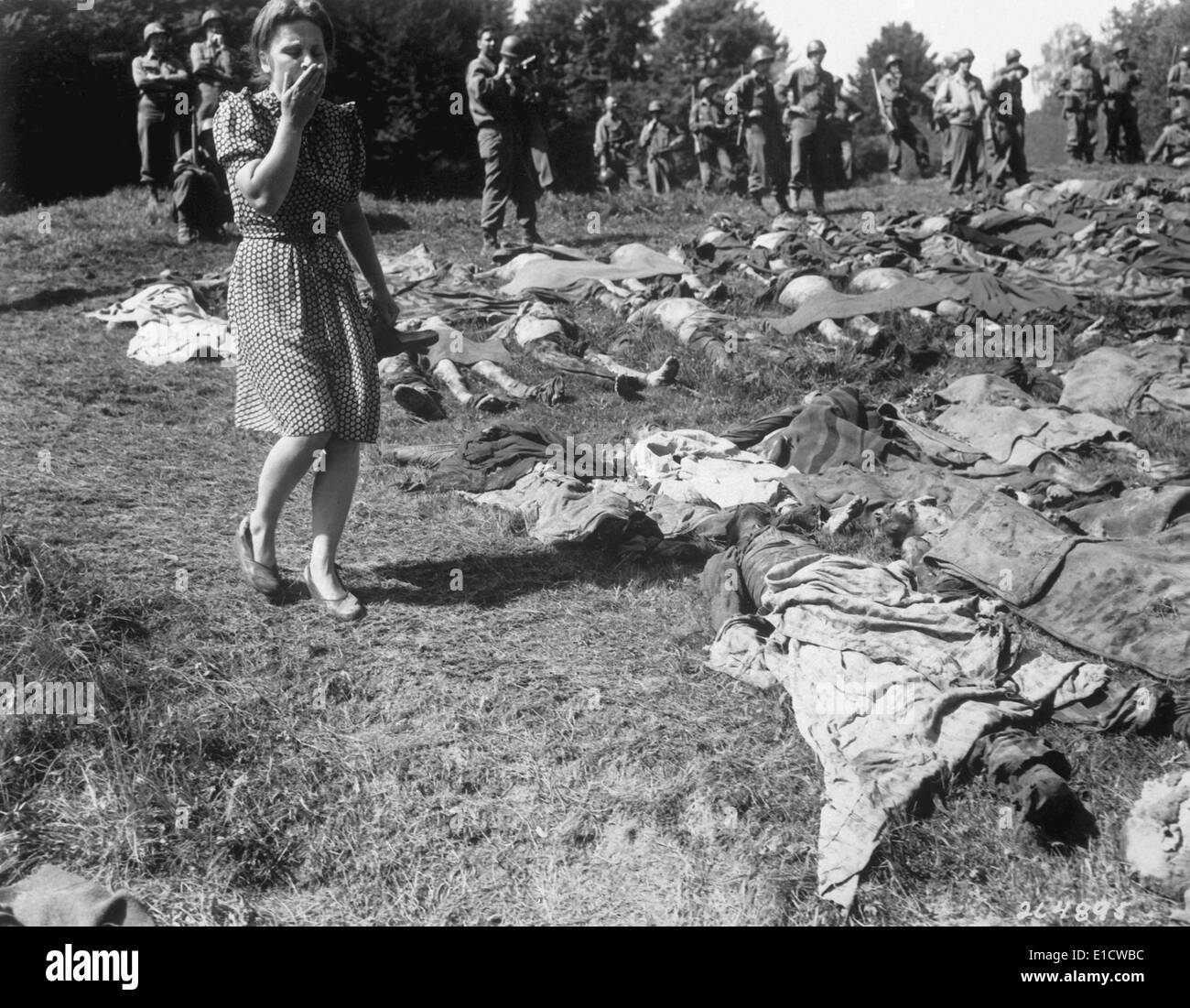 A German women walks past the exhumed bodies of some of the 800 slave workers. They were murdered by SS guards at Flossenburg Stock Photo
