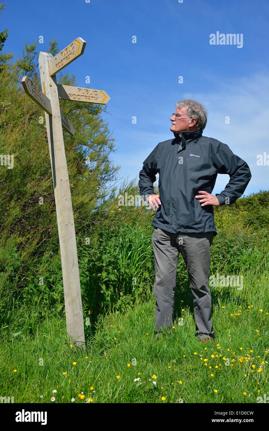 Man making a choice of direction standing beside a wooden public foothpath signpost (finger post)  at Snow Hill, West Wittering, West Sussex,UK Stock Photo