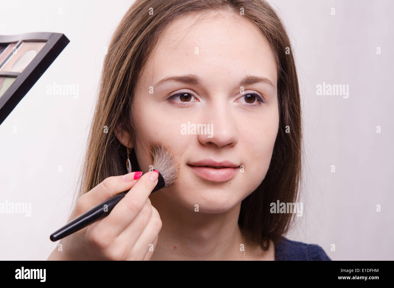 Makeup artist applies powder on the face of a beautiful young girl in ...