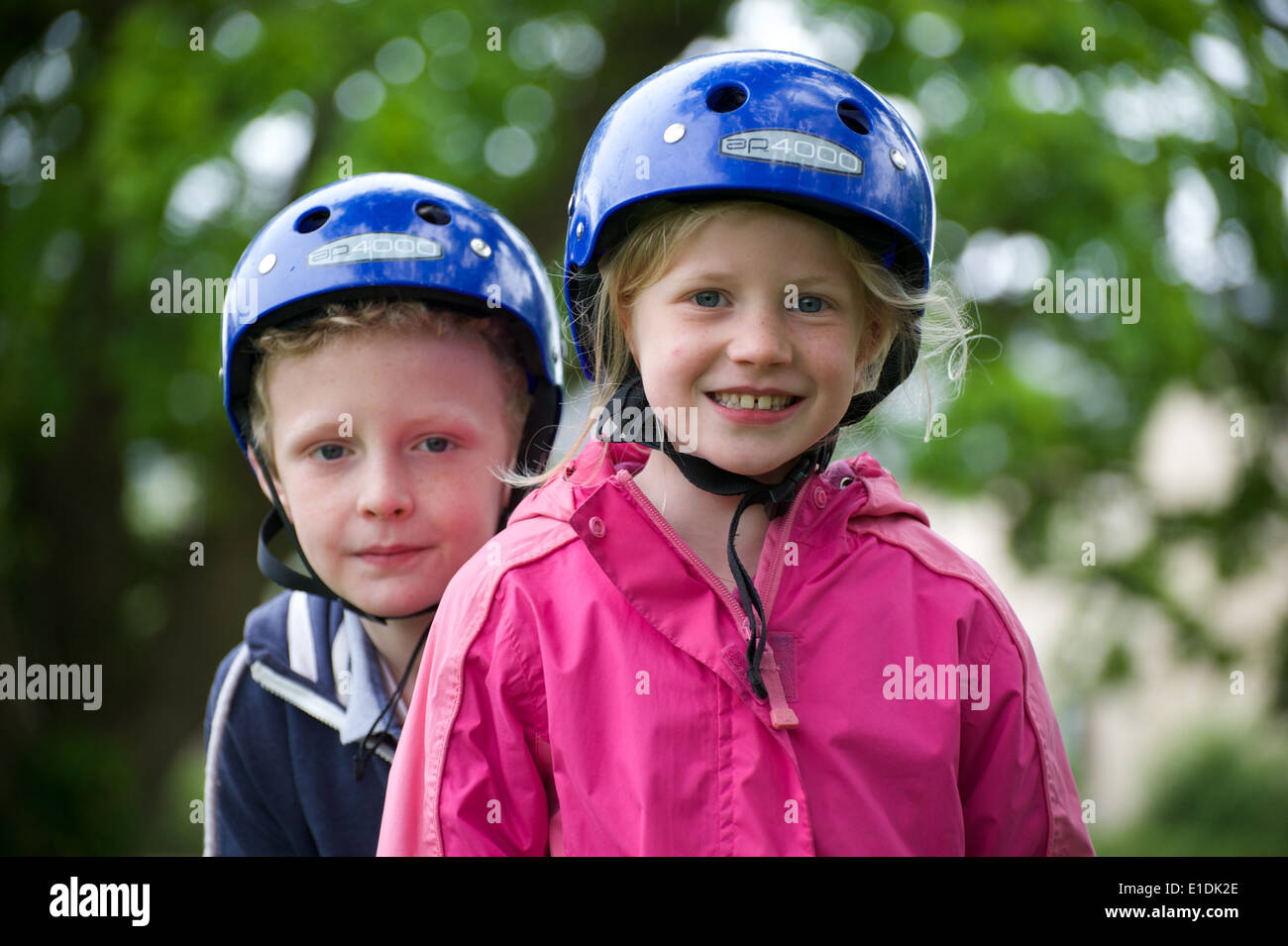 Two young blonde children wearing helmets get ready for some outdoor activity sport Stock Photo