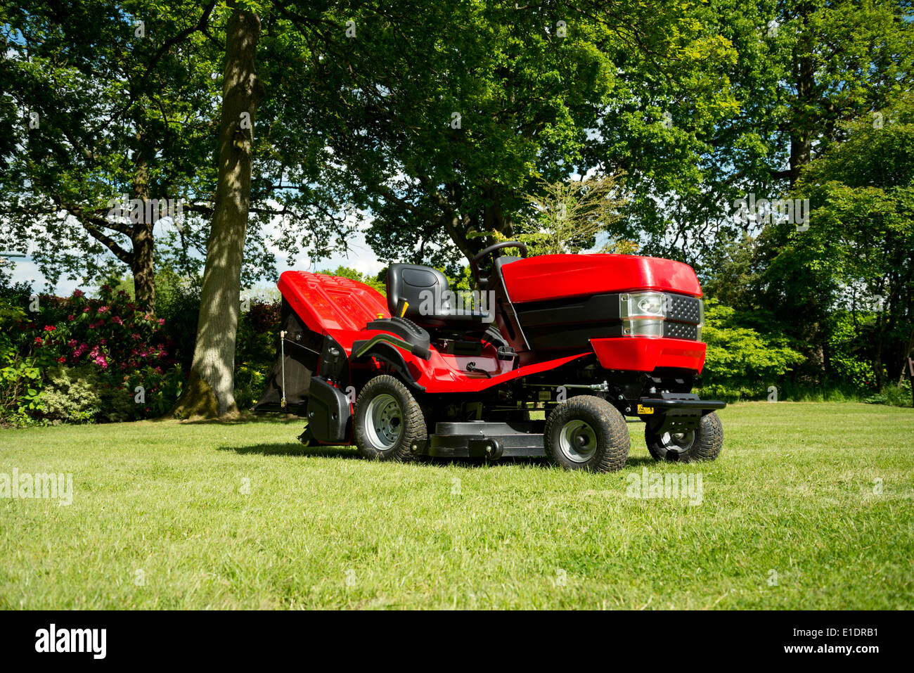 Red garden tractor, or ride on mower, in an verdant garden. Stock Photo
