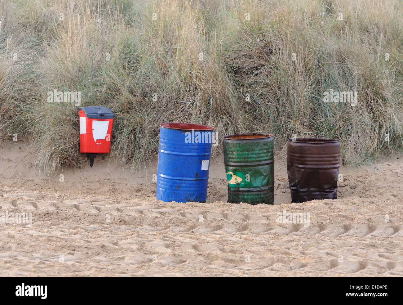 Empty red,  green and blue oil drum rubbish bins on the beach in front of marram grass covered dunes. Hunstanton, Norfolk, UK. Stock Photo