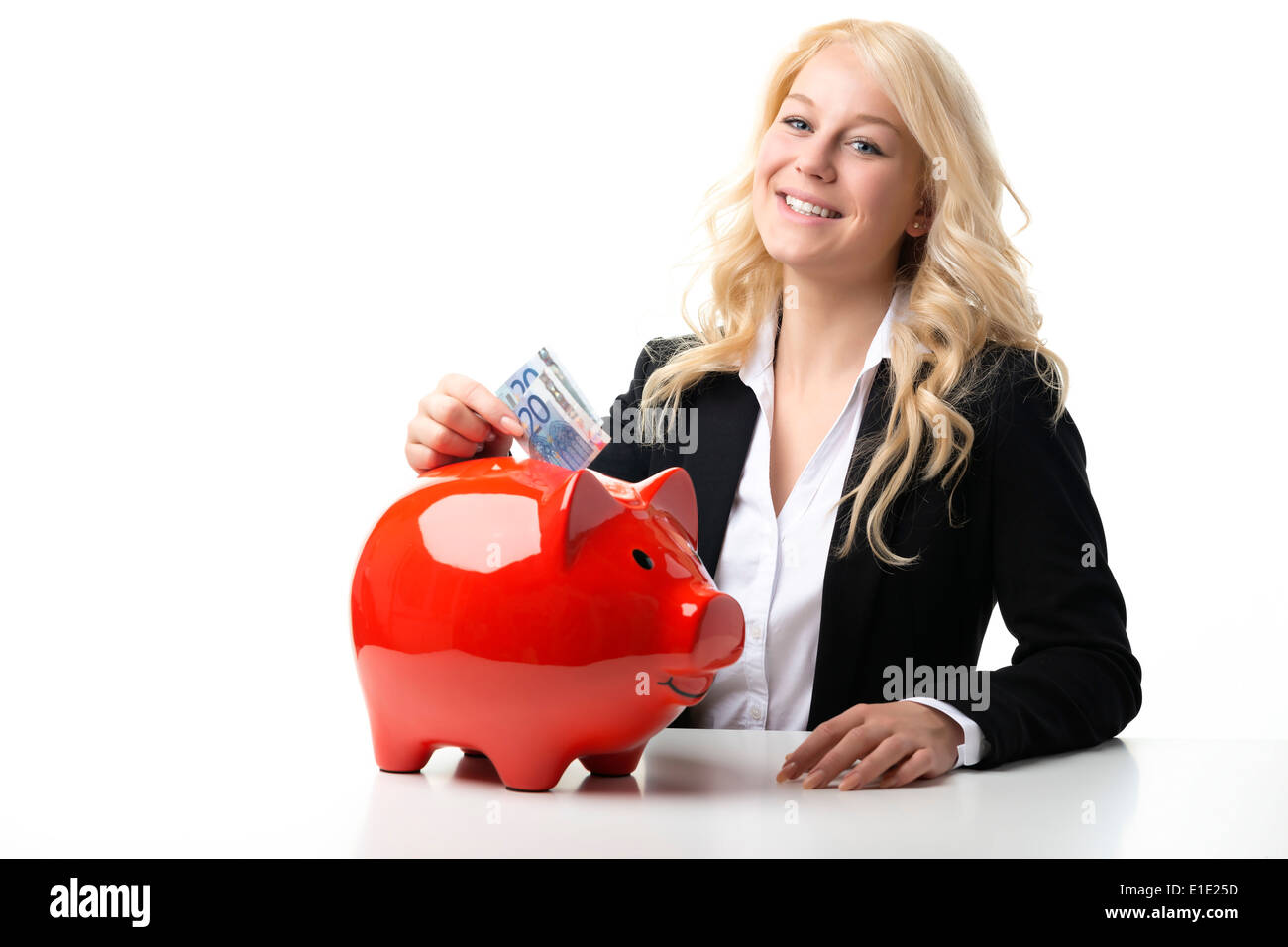 Happy blond women sitting at a table and throwing euro banknotes in a red piggy bank Stock Photo