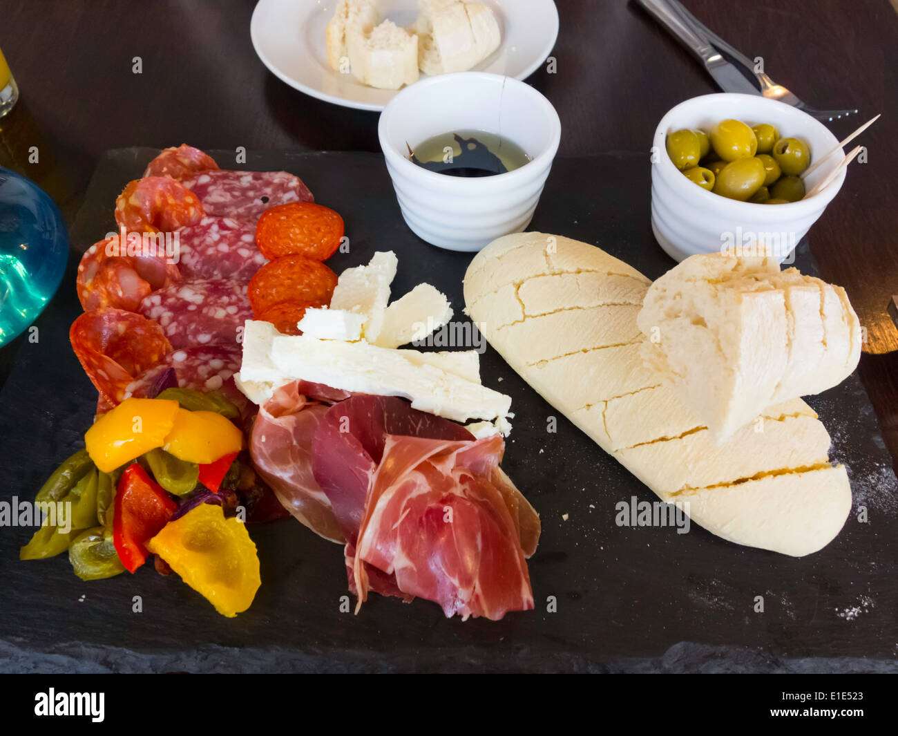 Lunch time snack meal deli platter cold meats mozzarella cheese Ciabatta bread olive oil olives and pickled peppers Stock Photo