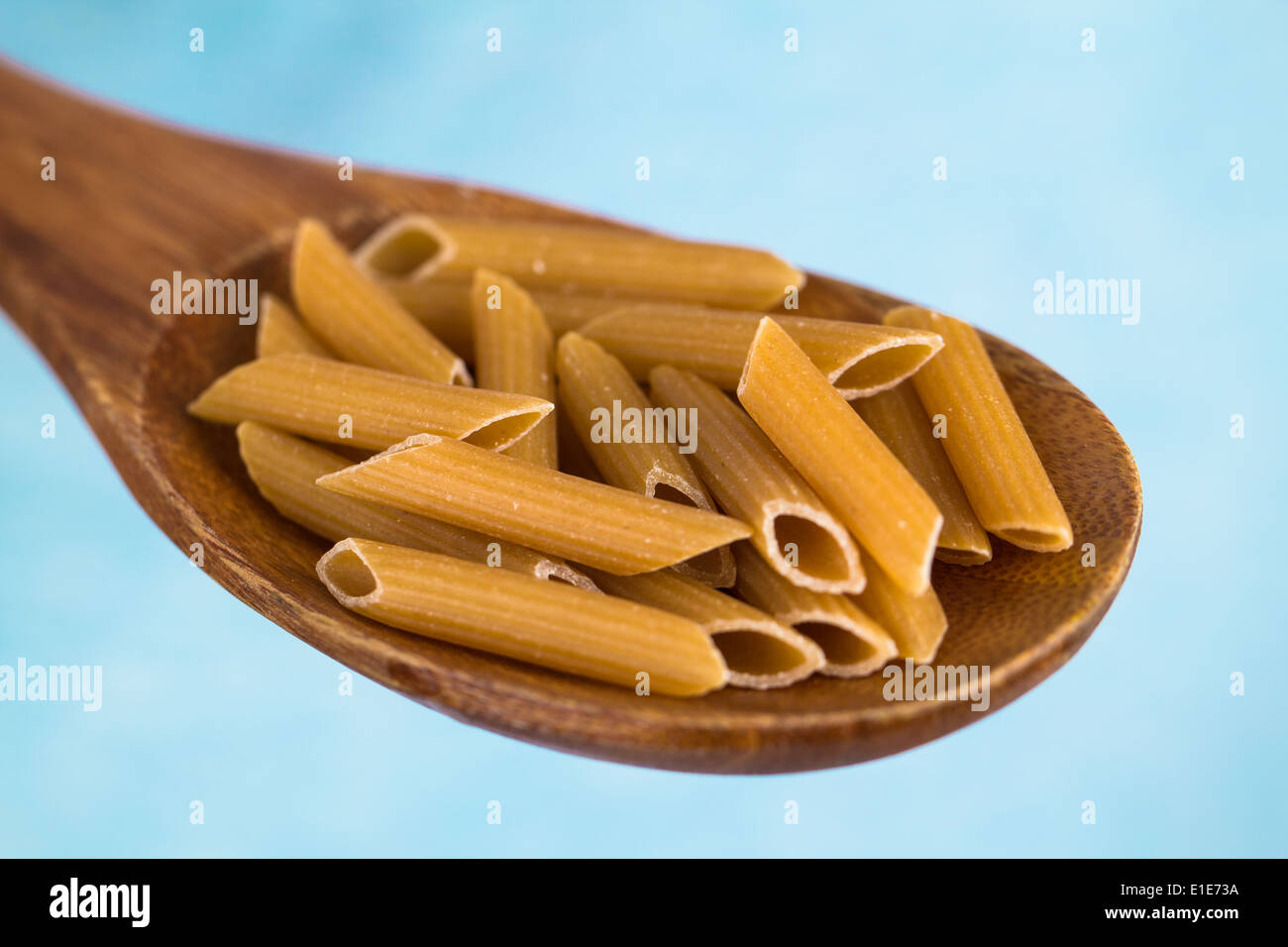 A hand holding a wooden spoon with wholemeal penne pasta Stock Photo