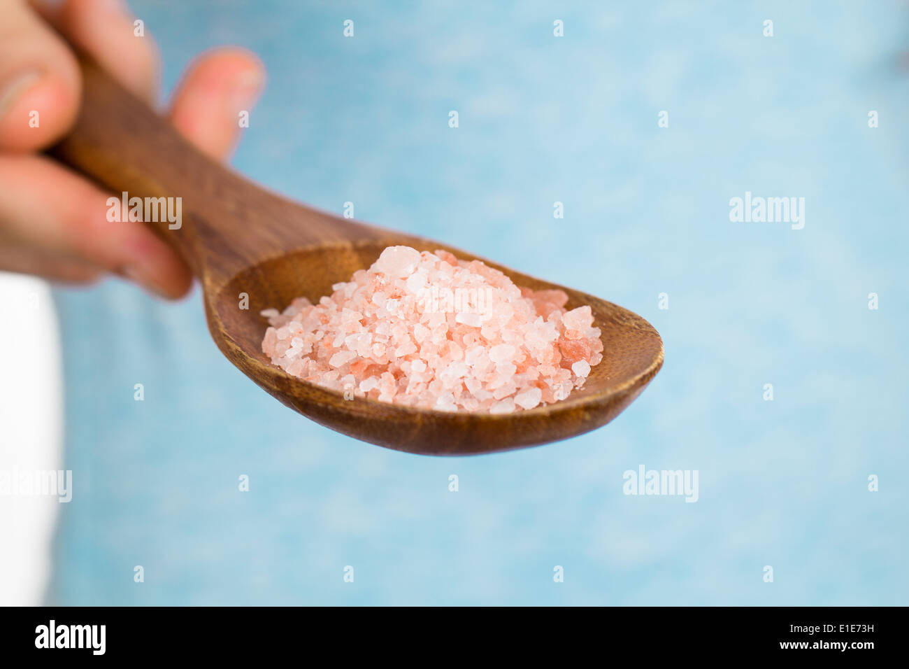 A hand holding a wooden spoon with Himalayan rock salt. Stock Photo