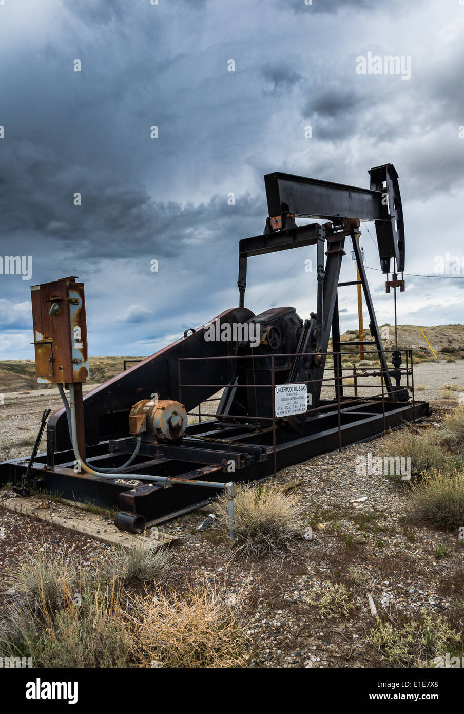 An idled oil pump-jack under dark stormy clouds. Wyoming, USA. Stock Photo