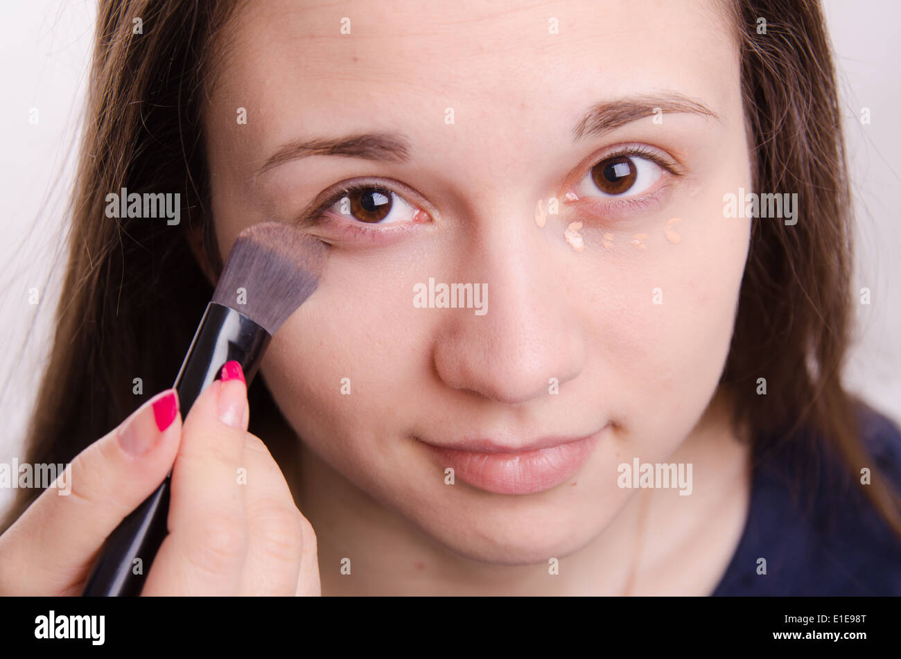 Makeup artist applies foundation of a beautiful young girl in the