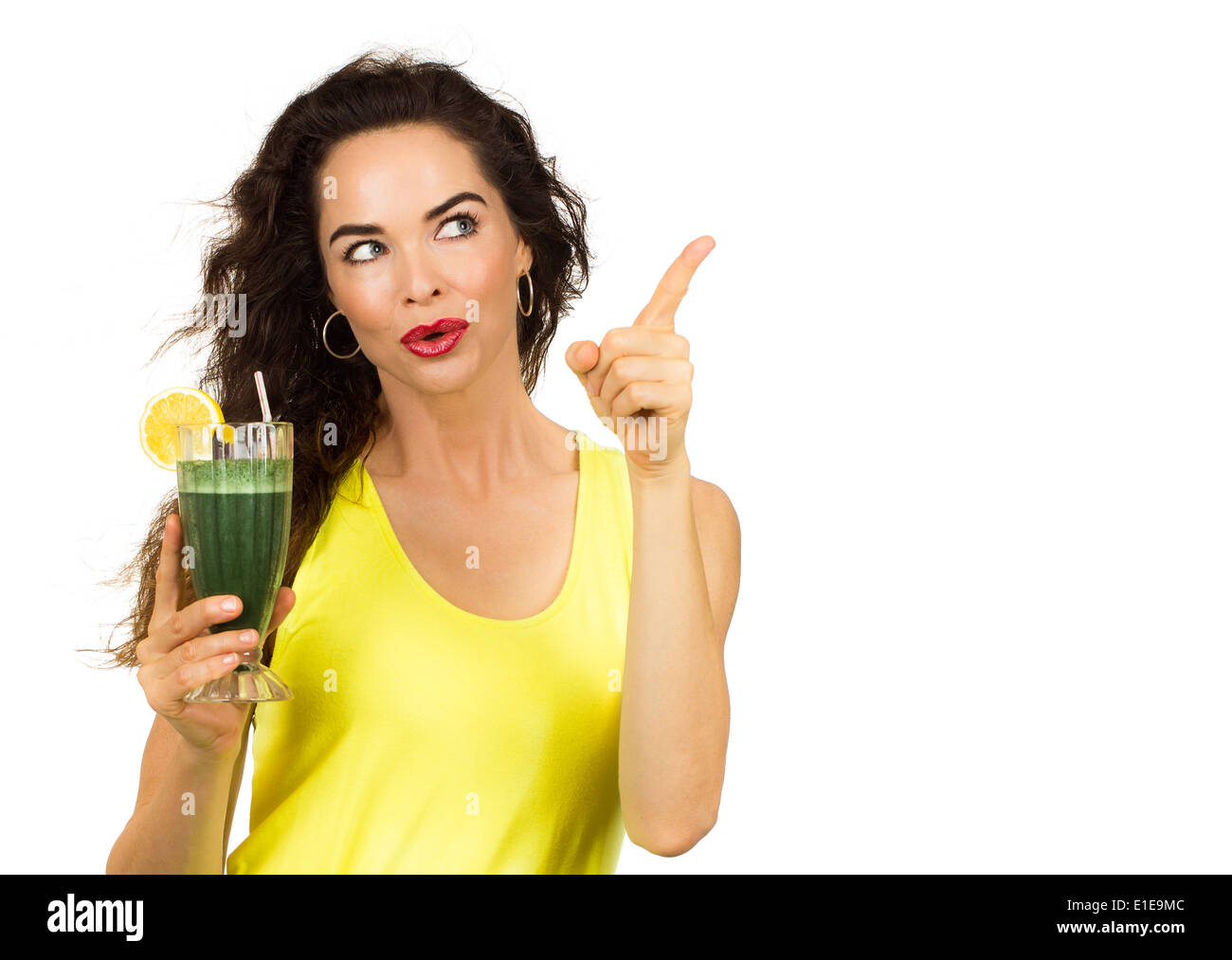 Beautiful healthy woman holding an organic green smoothie and pointing at copy-space. Isolated on white. Stock Photo