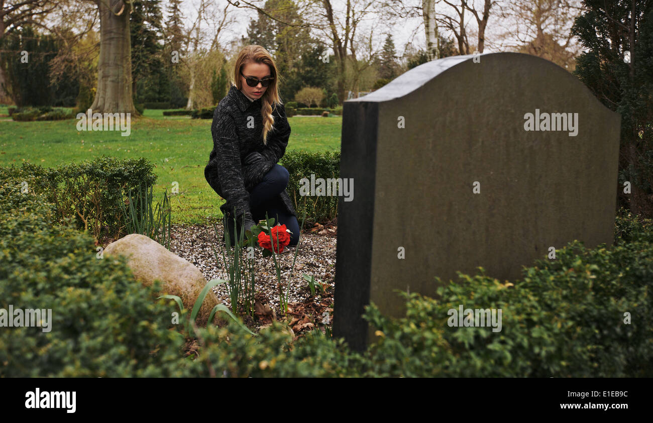 Young woman sitting at the gravestone of her family member Stock Photo