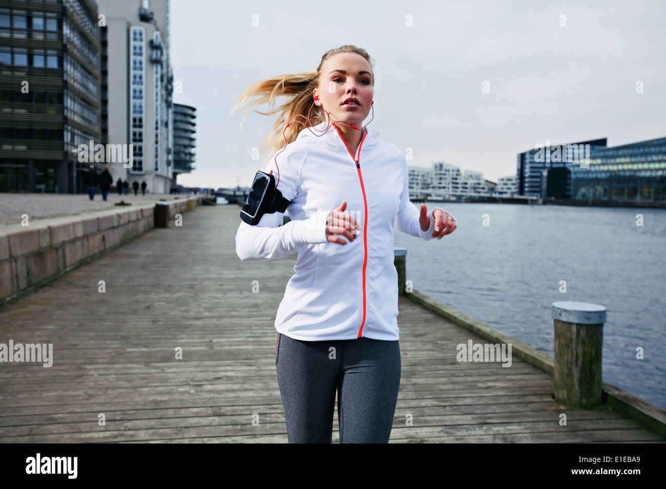 Fit young woman running on the boardwalk along river. Caucasian female athlete training outdoors by the waterfront. Stock Photo