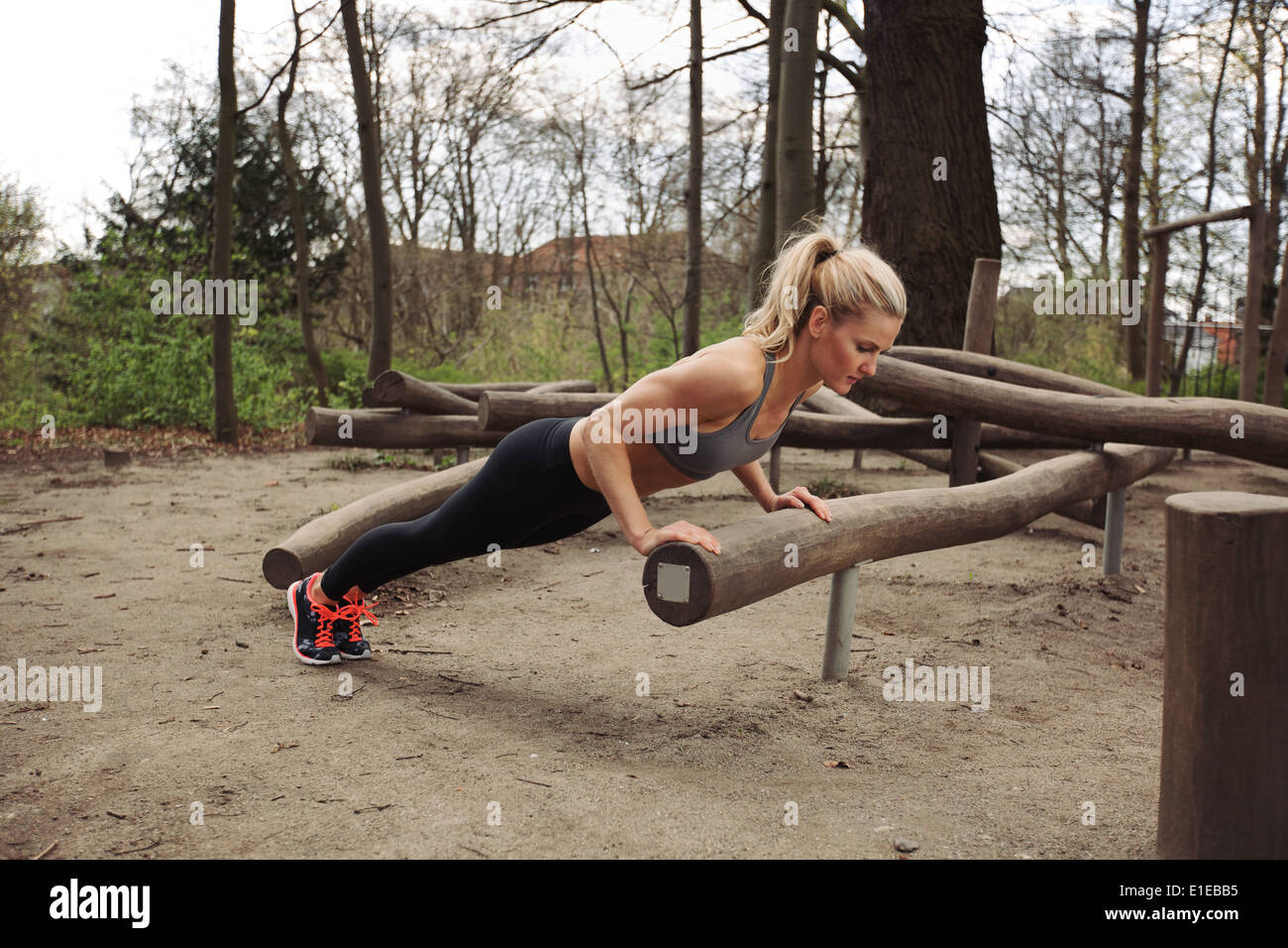 Tough young woman doing pushups on a log at park. Fit young woman exercising in woods. Stock Photo
