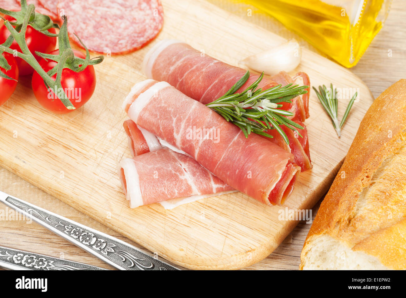 Prosciutto, bread, vegetables and spices on wooden table Stock Photo