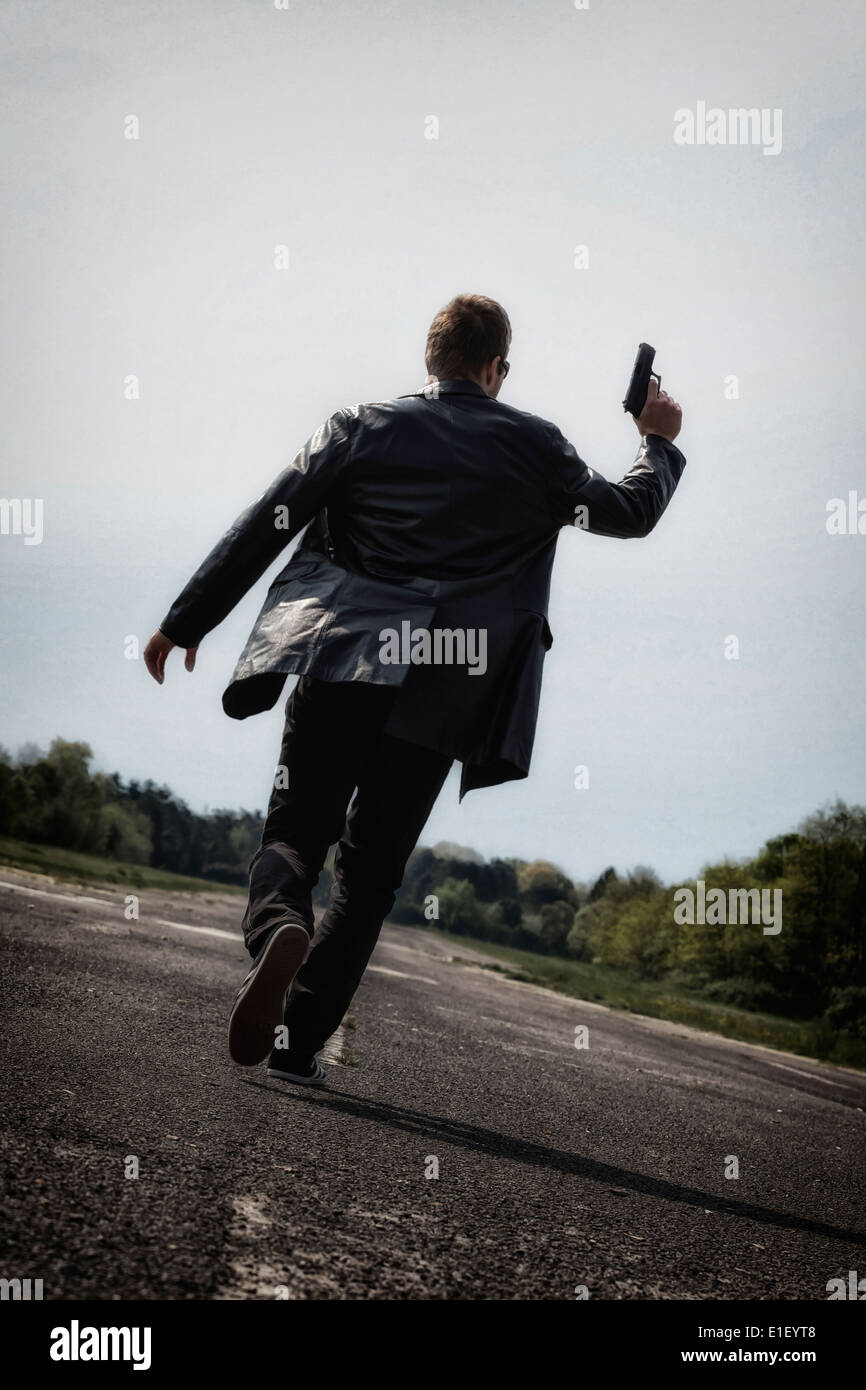 a man running on an abandoned street with a gun Stock Photo