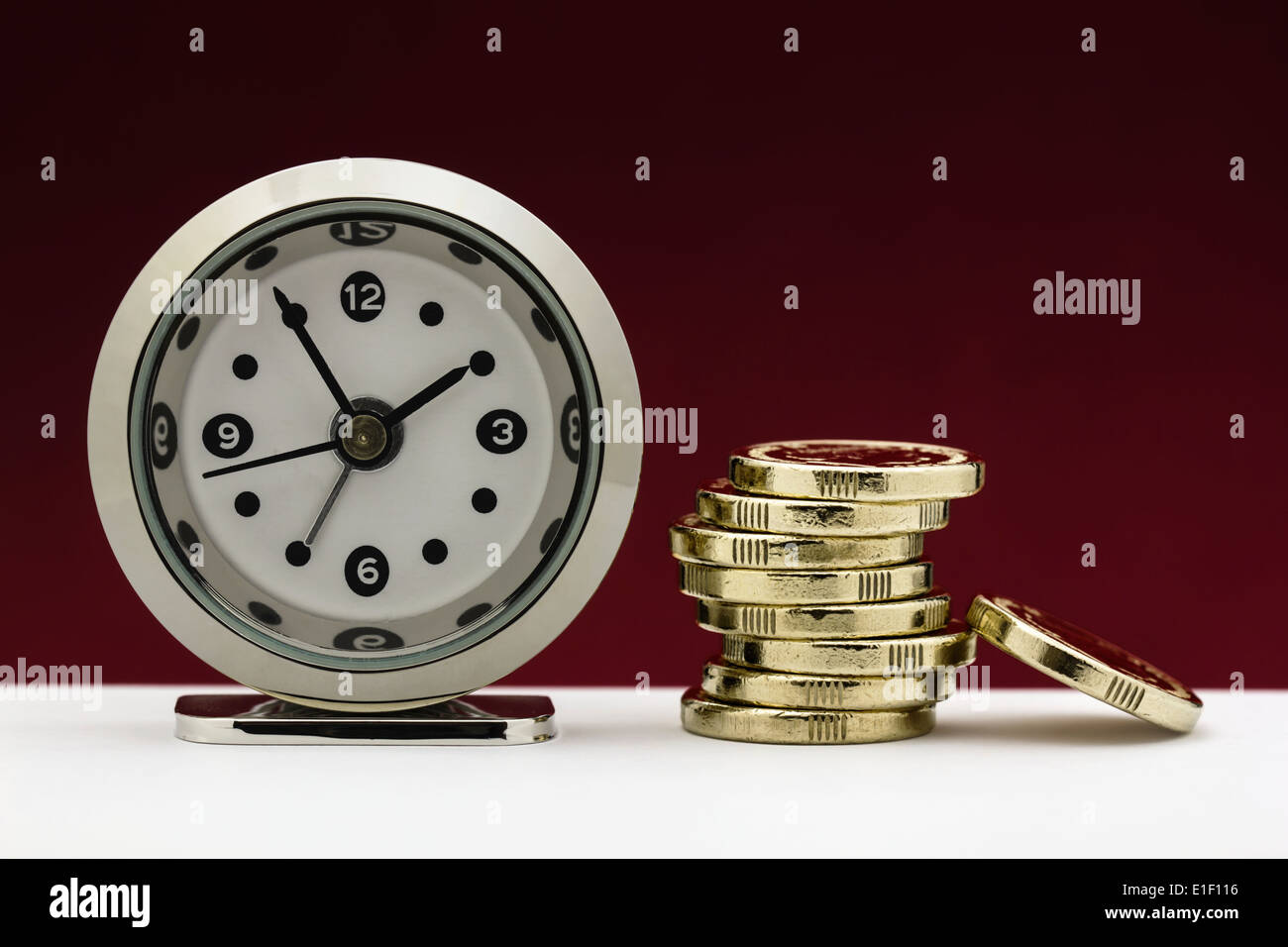 Clock with a stack of gold coins illustrating the concepts of time is money or financial deadline/pressure. Stock Photo