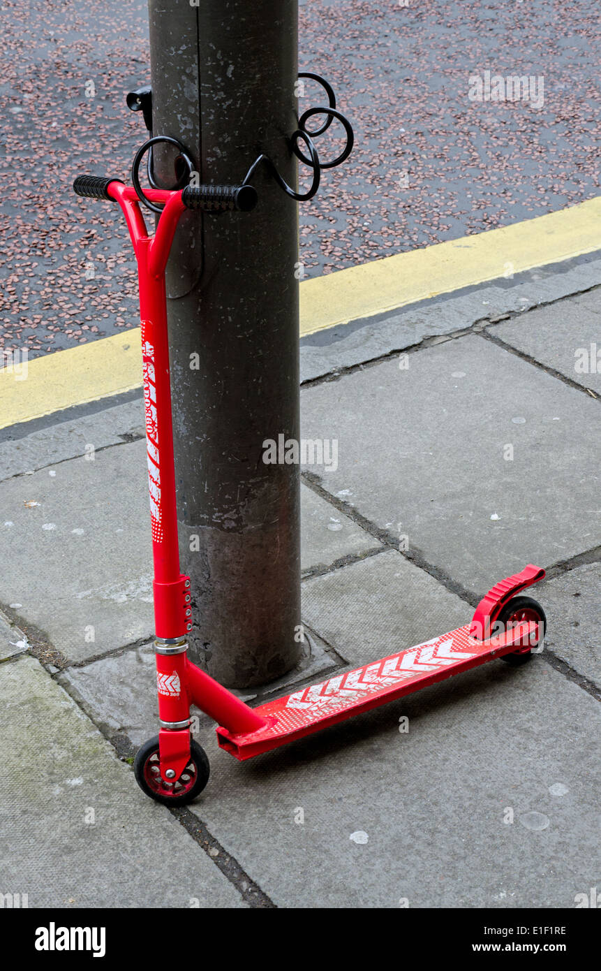 A red micro scooter secured to a post. Stock Photo