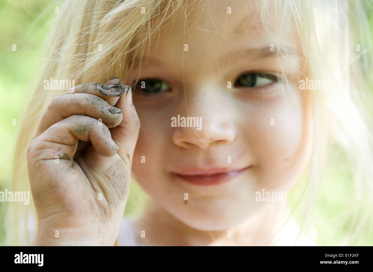 Child blond girl holding worm outside in the garden, portrait, summer