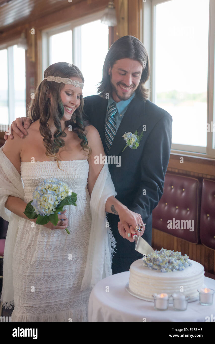 Boho couple cutting their wedding cake inside a riverboat Stock Photo