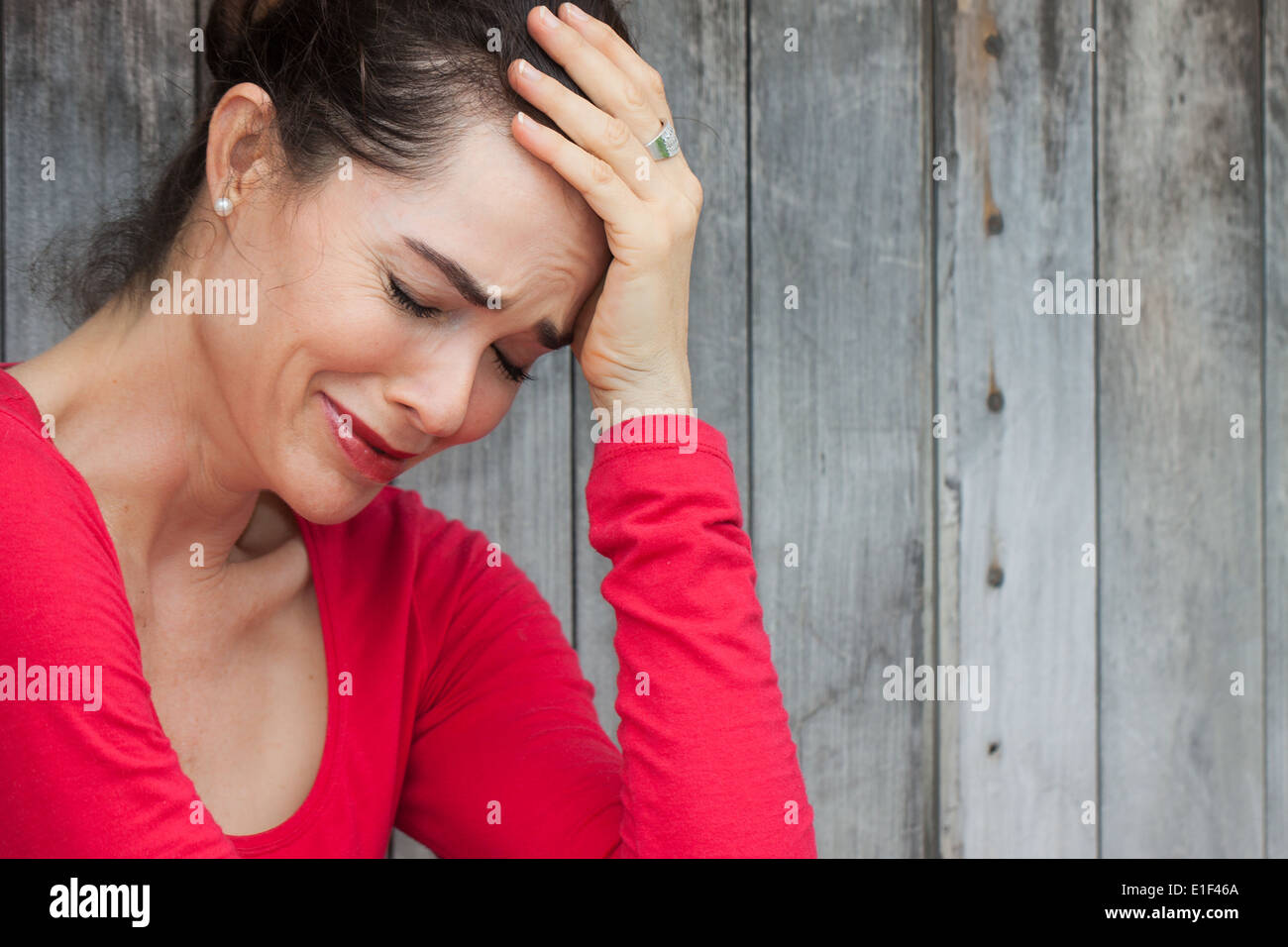 A very upset and lonely woman sitting down crying against a wall Stock Photo