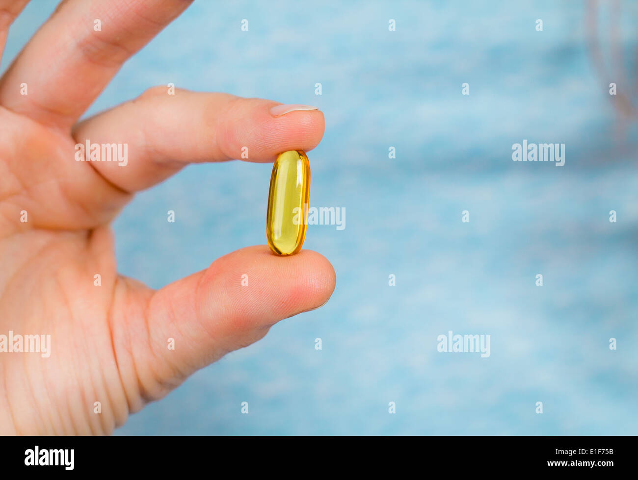 Close-up shot of fingers holding a fish oil capsule. Stock Photo