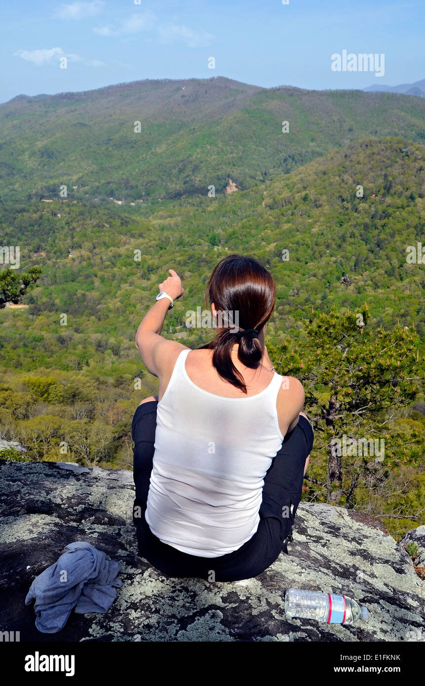 A woman hiker sitting on a mountain overlook pointing at a landmark. Stock Photo