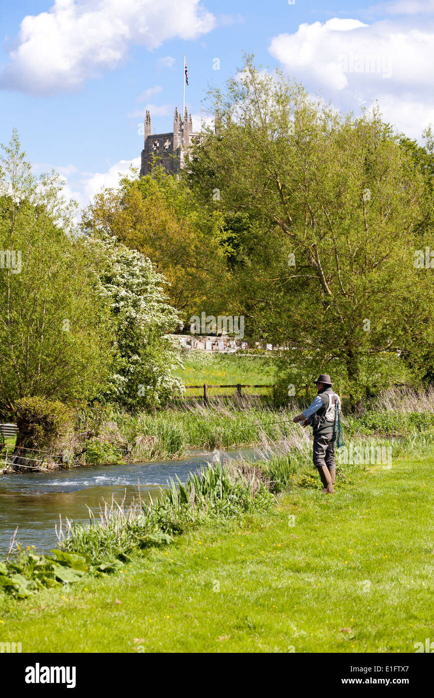 Fly fishing for trout on the River Coln opposite St Marys church in the Cotswold town of