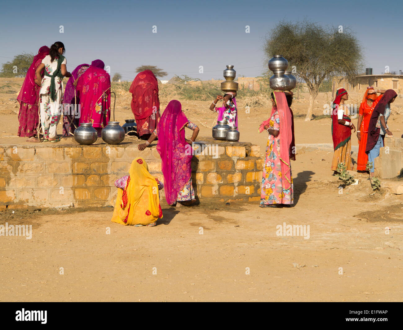 India, Rajasthan, Jaisalmer, Thar Desert, Khuri, women dressed in colourful saris collecting water from village well Stock Photo
