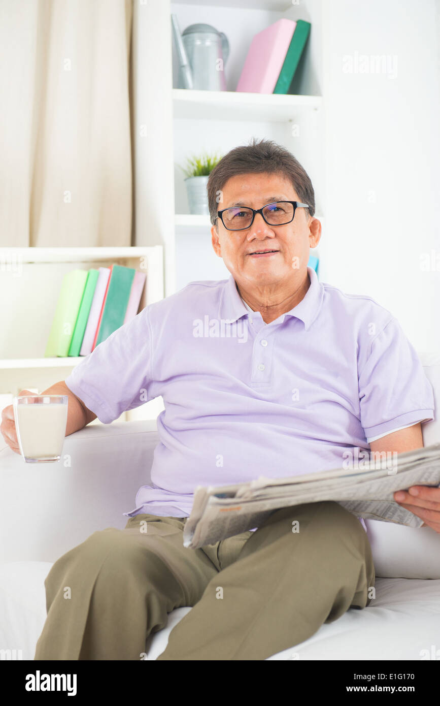 senior asian chinese reading newspaper and drinking milk on a sofa in home Stock Photo