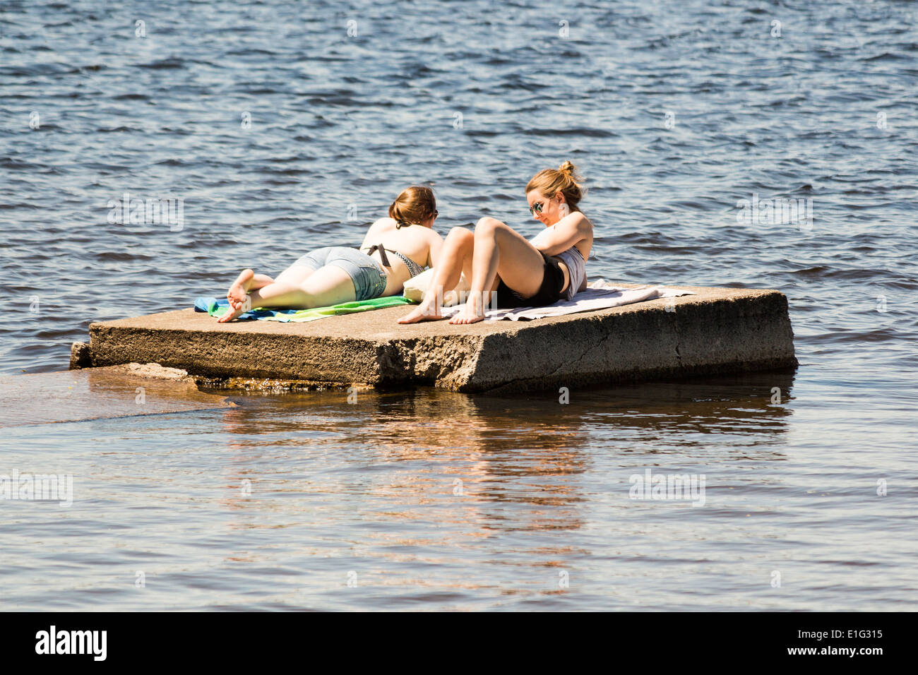 Two women sunbathing on a concrete dock floating on a lake Stock Photo