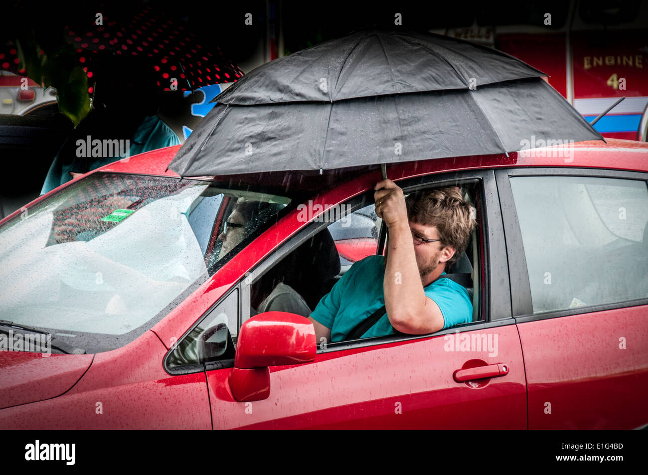 Keeping dry, this man while watching a parade in a rain storm rolled down his window , put up an umbrella better hear the music. Stock Photo