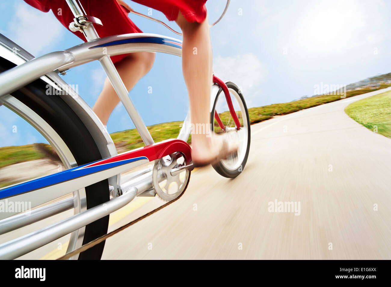 A unique angle of a man riding his beach cruiser down the bike path in swim trunks and sandals. This rig shot gives a sense of s Stock Photo