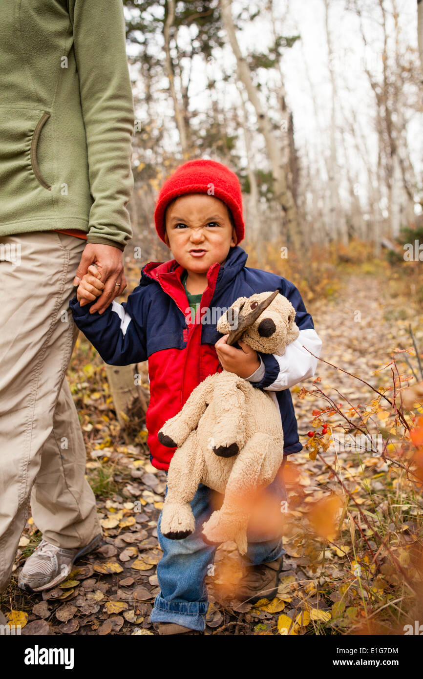 Boy holding mothers hand holds stuff animal on a leaf covered trail Stock Photo